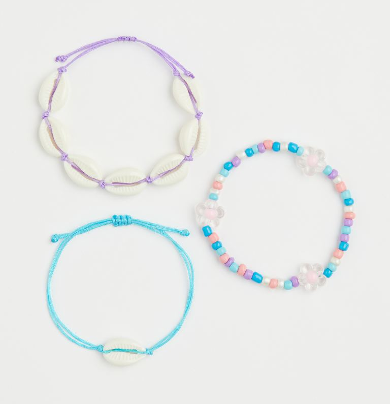 Purple string bracelet with white shells, blue string bracelet with single shell, blue, purple, pink, and white beaded bracelet with white daisy beads on a white background