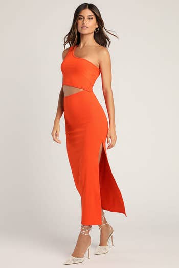 Woman in an asymmetric orange gown with cut-outs poses, paired with strappy heels. Perfect for gala shopping