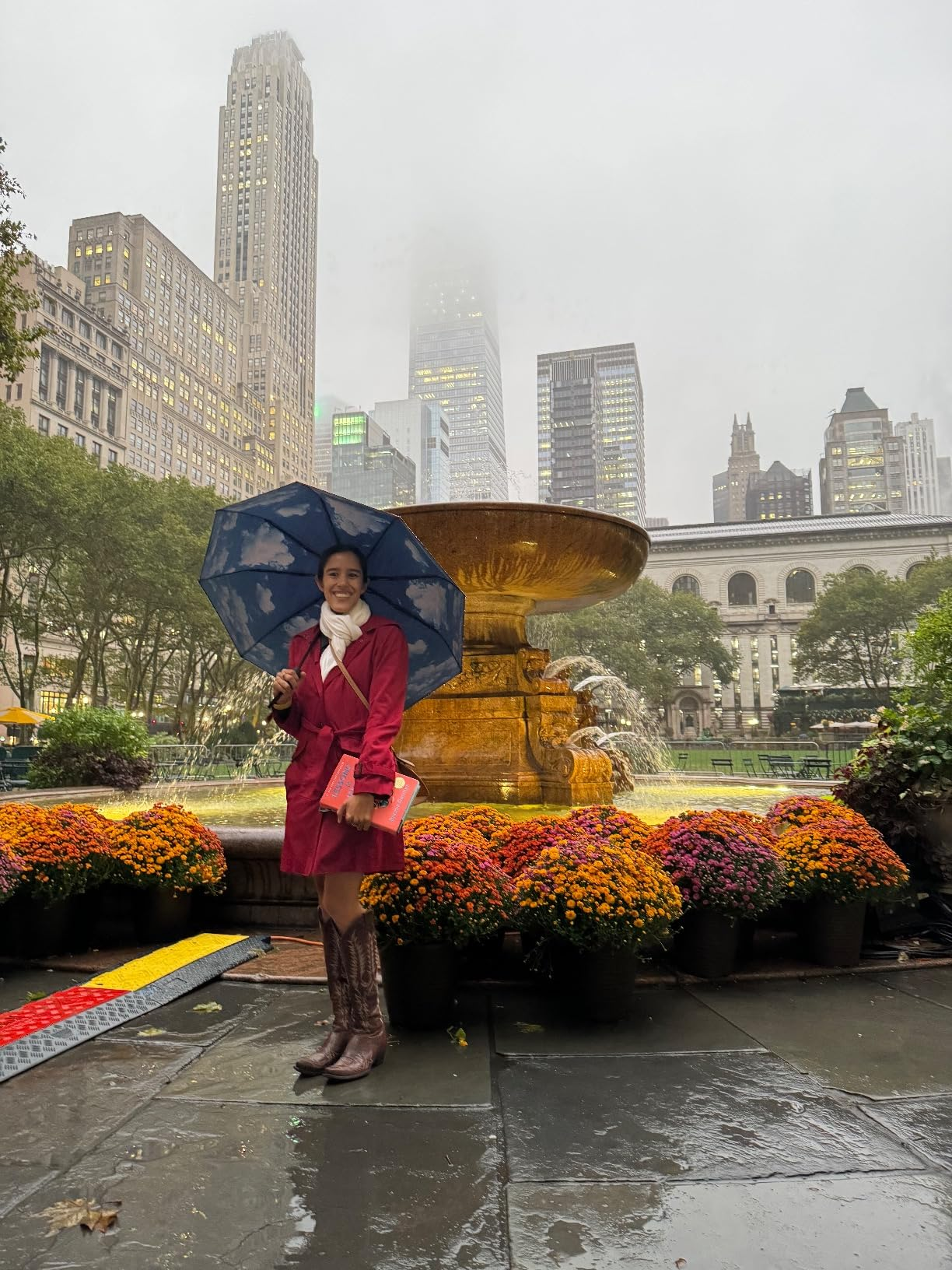 reviewer smiling and using the umbrella with cloud designs underneath, posing in front of a foggy city-scape