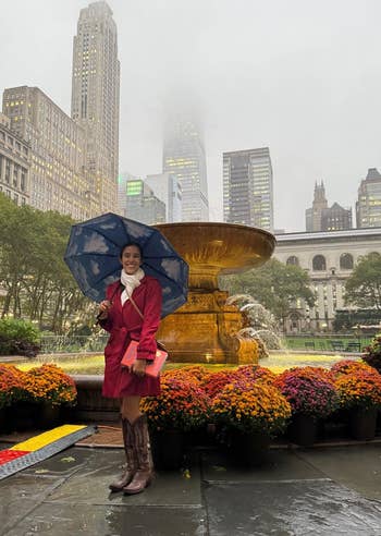 reviewer smiling and using the umbrella with cloud designs underneath, posing in front of a foggy city-scape
