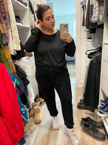 Person trying on a black outfit with sneakers, taking a selfie in a mirror in a clothing store