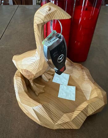 Wooden bird-shaped cardinal  holder with a acceptable   of car   keys, placed adjacent  to stacked reddish  cups and a fewer  wide   circular stickers connected  a table