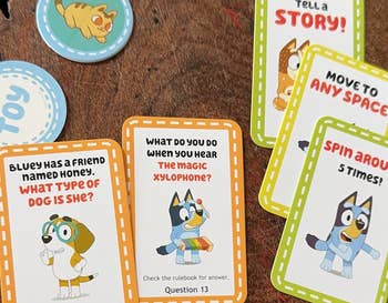 Various Bluey-themed game cards are spread out on a table, featuring questions and instructions for players