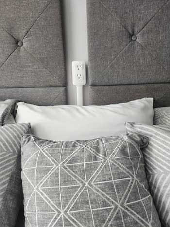 Bantal bermotif geometris di tempat tidur menonjolkan dekorasi kamar tidur modern dengan stopkontak yang terlihat di latar belakang