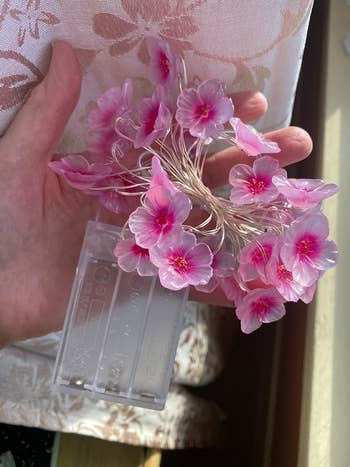 Reviewer holding pink flower shaped fairy string lights with clear empty battery pack