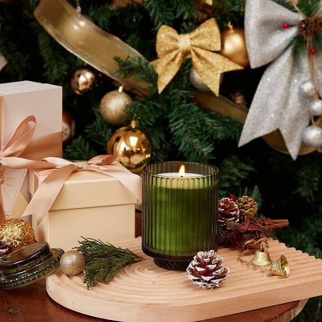 glass candle in decorative jar beside presents and christmas tree