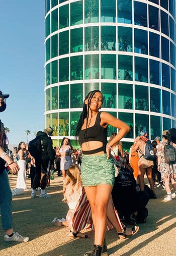 reviewer at festival in a black crop top, green patterned shorts, and lace-up boots, with others around her