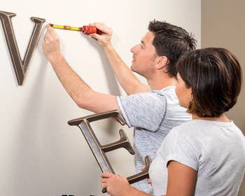 two people working together to use tool to hanging wall art on walls