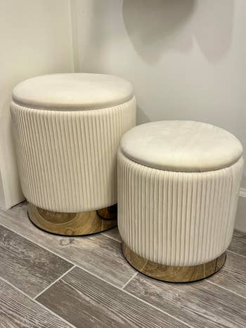 Two pleated fabric ottomans with wooden bases displayed on a tiled floor, suitable for modern home decor