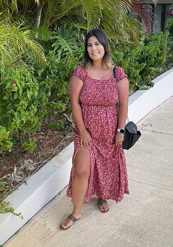 reviewer in a floral dress with a high-low hemline, posing on a sidewalk. She is accessorized with a watch and sandal heels