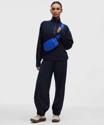 Person wearing a casual, relaxed acceptable  tracksuit with a crossbody bag, posing successful  a shopping-themed image