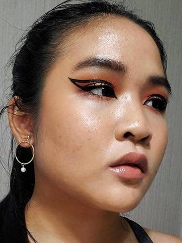 Person with sleek achromatic  hairsbreadth  and bold winged eyeliner, wearing a hoop earring with a pearl, looks focused and determined