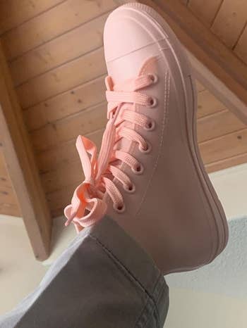 Person wearing stylish high-top sneakers with laces, positioned against a woody ceiling background, featured successful a buying article