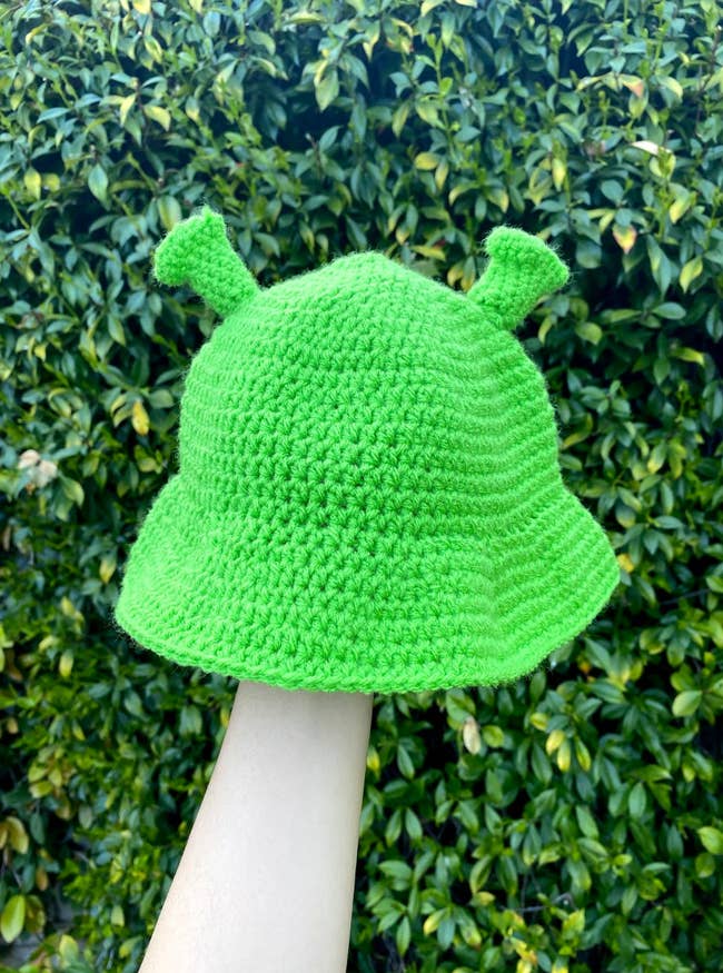 Model holding lime green ogre-shaped crochet bucket hat
