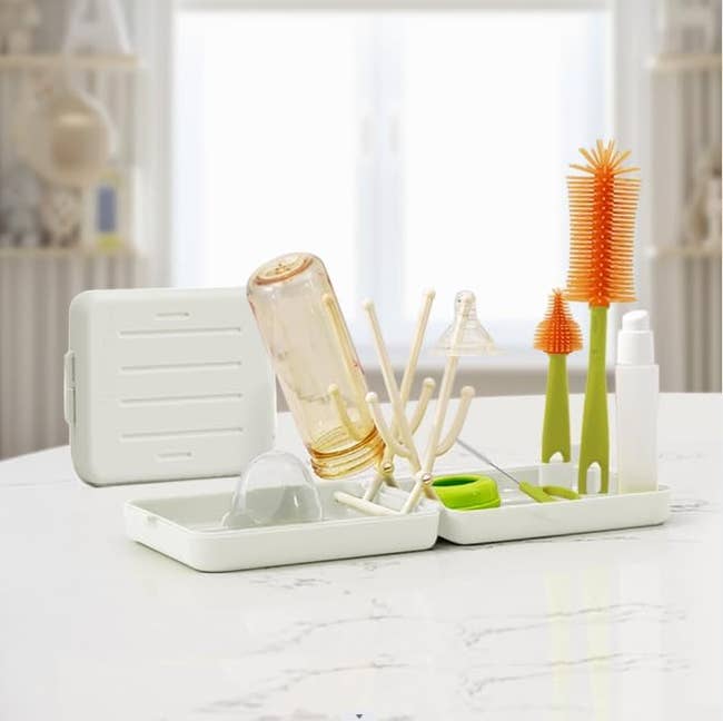 Drying rack on a kitchen counter with various baby bottle cleaning tools, including a clear bottle, brushes, and drying pegs