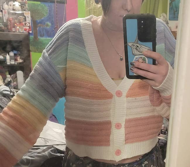 Person taking a reflector selfie wearing a striped pastel cardigan with ample buttons, holding a telephone with a popular civilization plan connected the case