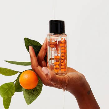 Person holding a clear bottle of skincare product beside an orange and leaves