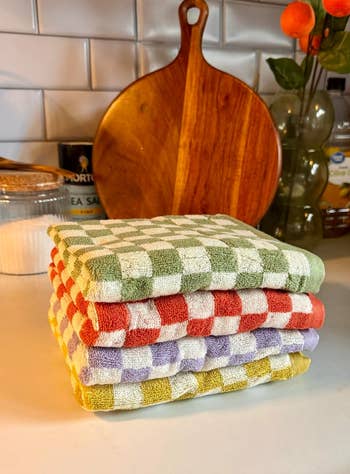 Stacked checkered kitchen towels on a counter with cooking utensils in background