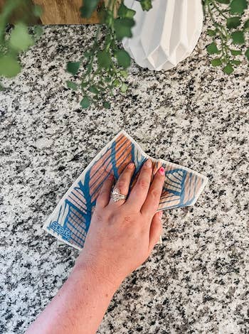 Hand wiping a granite countertop with a patterned cloth