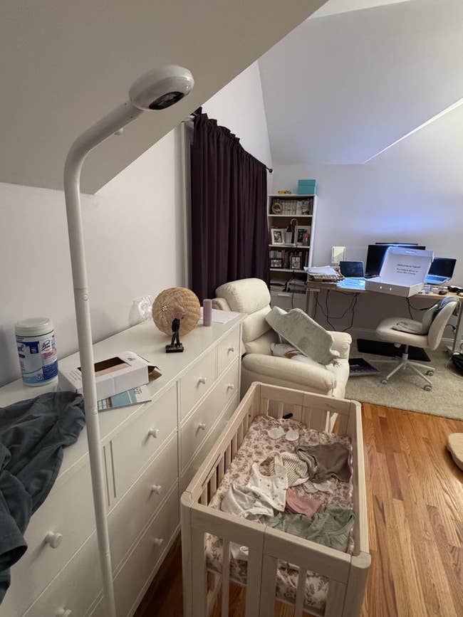 Cozy nursery setup with crib, dresser, and machine desk. Bright lamp and comfy seat successful room