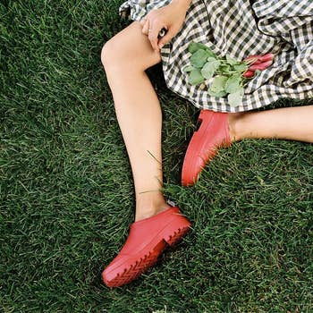 Person lying connected  writer  wearing a checkered dress, holding radishes, and wearing reddish  clogs. Relaxed, garden-themed scene