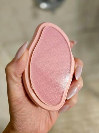 Hand holds a pinkish teardrop-shaped exfoliating ft record with a textured surface