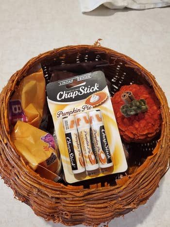 Basket with pumpkin-themed ChapStick and Halloween candy, featuring pumpkin pastry  flavor, alongside a decorative knitted pumpkin