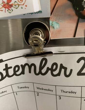 A calendar page hung by a metal magnet clip on a fridge 