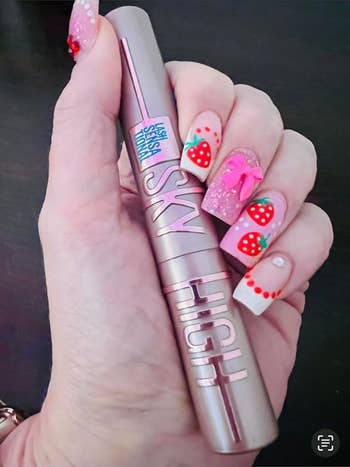 Hand holding a Sky High mascara conduit with strawberry nail art