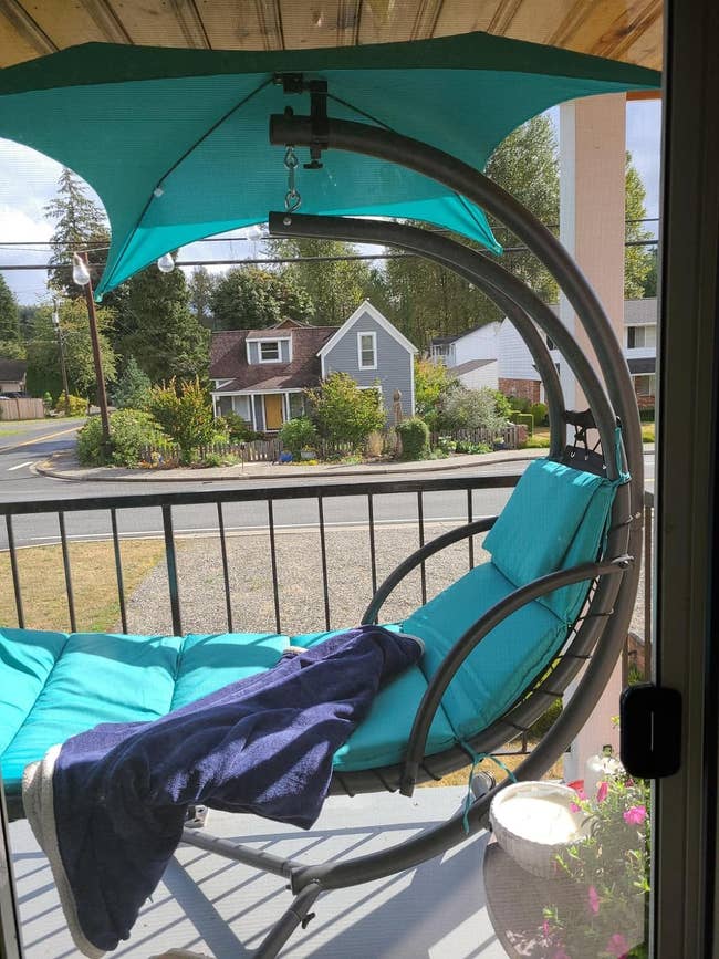 A porch swing with a canopy, cushions, and a throw blanket, overlooking a serene street view. Ideal for outdoor relaxation