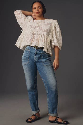 A idiosyncratic   successful  a lace apical  and jeans poses confidently. The outfit features a wide-sleeve apical  and relaxed-fit jeans, styled with sandals