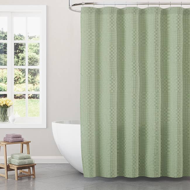 Bathroom with a modern, freestanding tub and a checkered ablution  curtain. A stack of folded towels is connected  a woody  stool adjacent   the tub