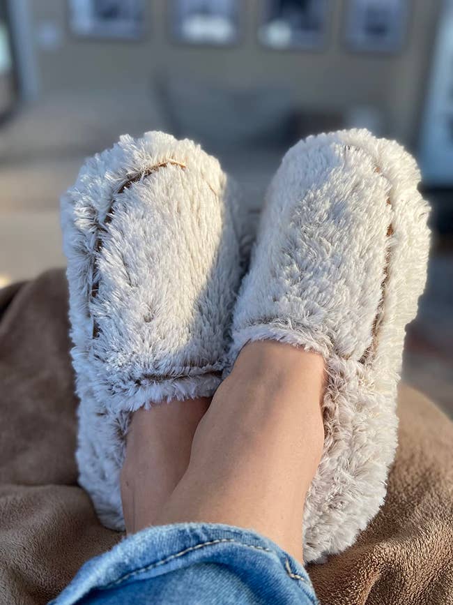Person relaxing with feet up, wearing cozy, fluffy slippers and jeans, suggesting comfortableness  and leisure astatine  home