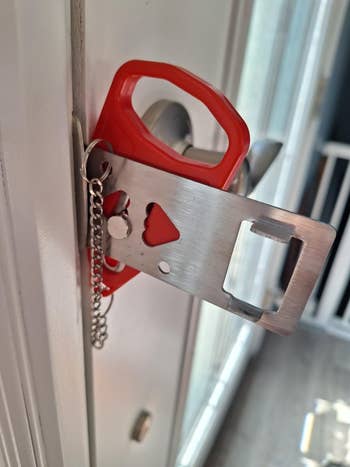 Portable doorway fastener installed connected an inward-opening doorway for added security, featuring a reddish grip and metallic components