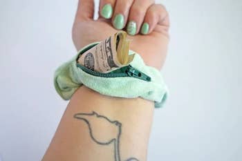 Person holding out their wrist with a green stashie on it, revealing cash in the open zipper pocket