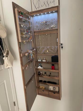 Wall-mounted jewelry cabinet with various necklaces, rings, and accessories neatly organized. Shelves hold watches and small boxes