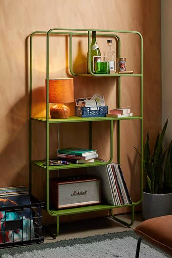 Modern green metal shelf with books, lamp, records, and various decor items, suitable for stylish home storage or display