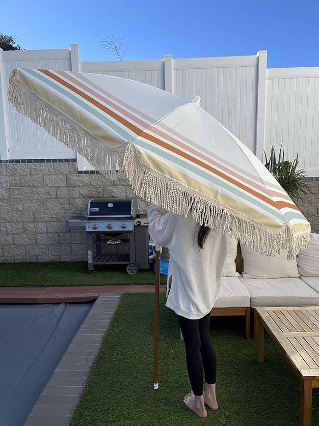 Person covered with a striped umbrella in a backyard