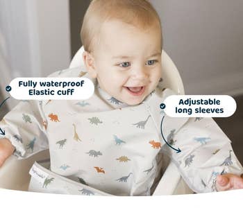 Baby wearing a bib with dinosaur print and long sleeves, text highlights features like waterproof and adjustable cuffs