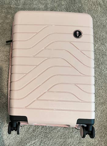 a BuzzFeed writer's light pink carry on suitcase