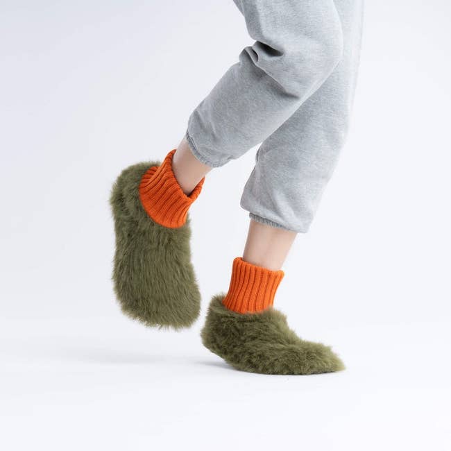 a pair of green furry slippers with an orange ribbed cuff