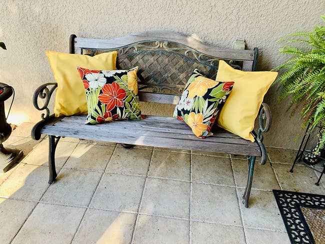 four pillows on a wooden bench, two yellow and two tropical-printed pillows