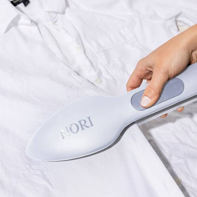 Hand using Nori handheld steamer on a white shirt, demonstrating easy wrinkle removal for clothing care