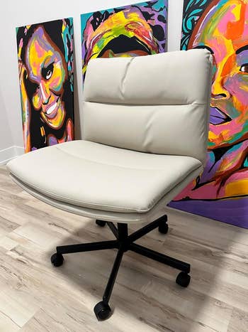 Modern office chair on wheels in front of two vibrant, abstract portrait paintings on a wooden floor