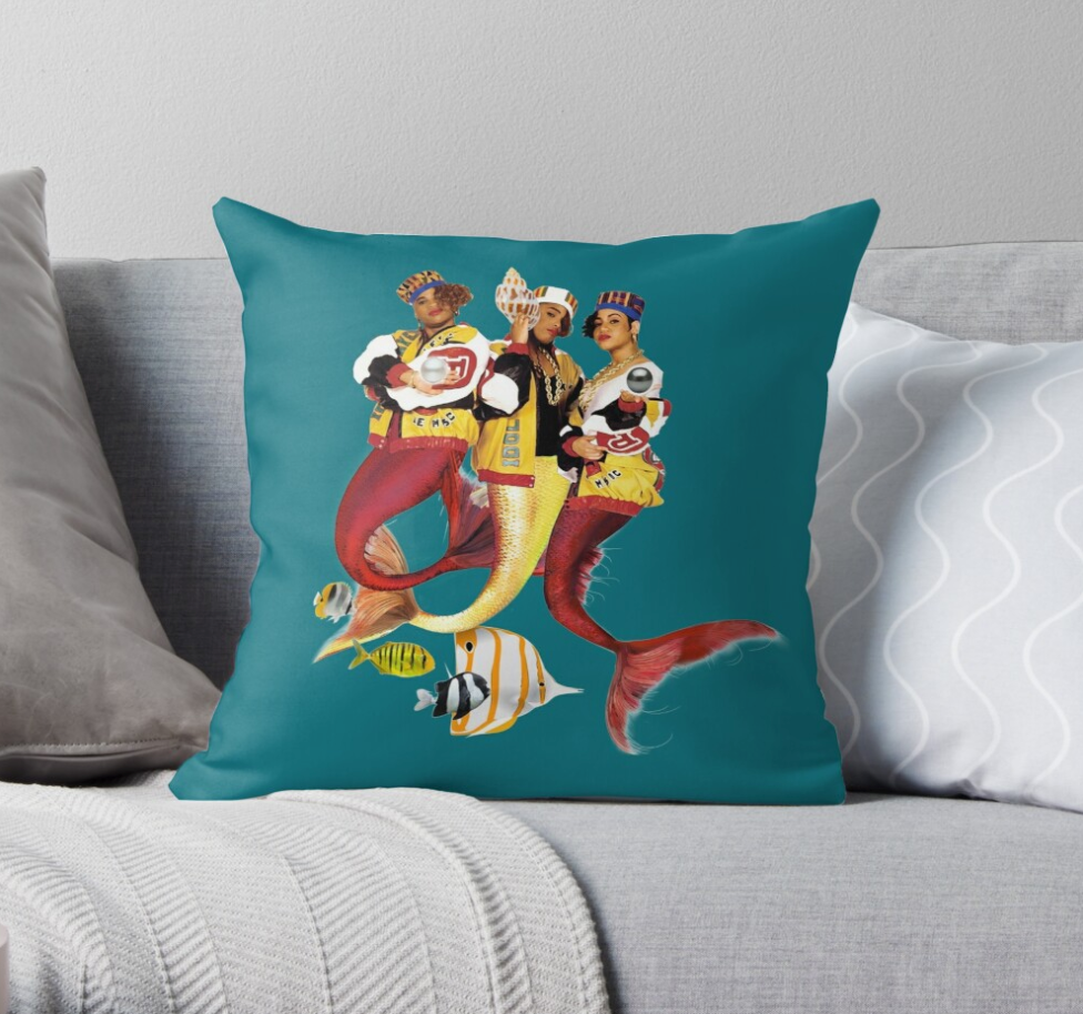 teal throw pillow with the three members of salt-n-pepa on it illustrated as mermaids with a few fish