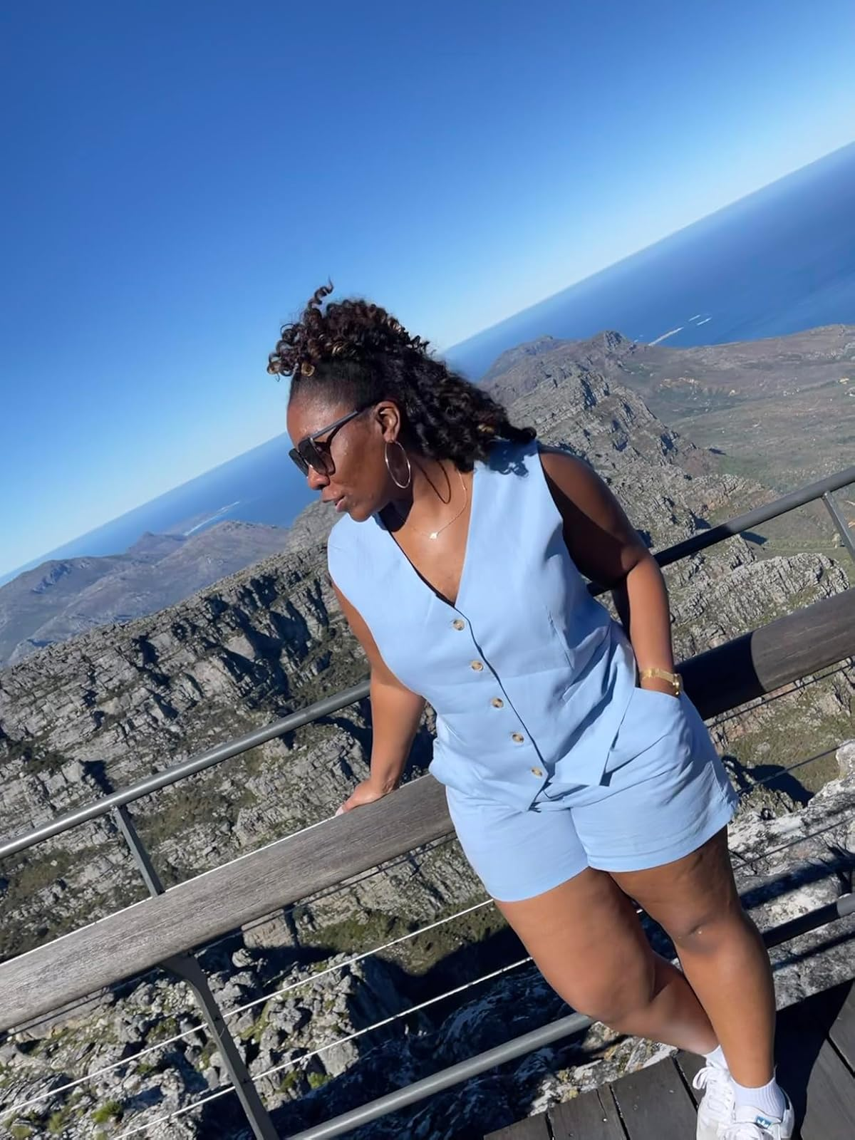 Person successful  sleeveless buttoned outfit and sunglasses leans connected  railing astatine  a scenic mountainous viewpoint nether  wide   sky