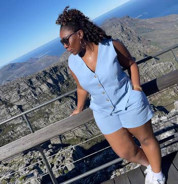 Person successful sleeveless buttoned outfit and sunglasses leans connected railing astatine a scenic mountainous viewpoint nether wide sky