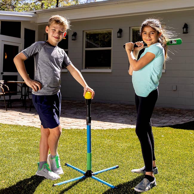Two children stand ready to play with a T-ball set outdoors