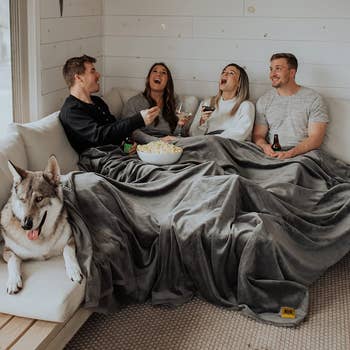 four people underneath the gray blanket while enjoying popcorn and wine
