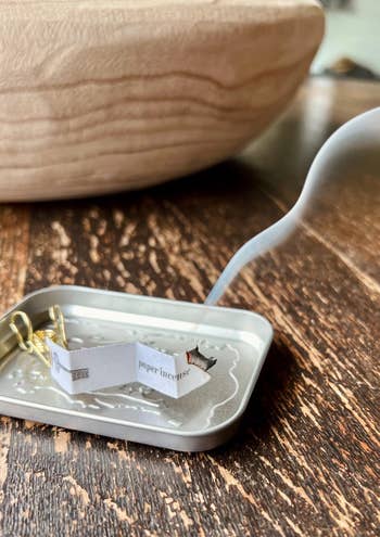 A small tray with a lit paper incense stick emitting smoke, set on a wooden table